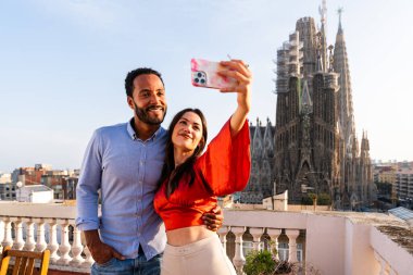 Sagrada Familia, Barcelona 'nın çatı katında buluşan çok ırklı, mutlu aşıklar şehir manzaralı bir terasta romantik aperatifler, turizm ve insan yaşam tarzı hakkında kavramlar