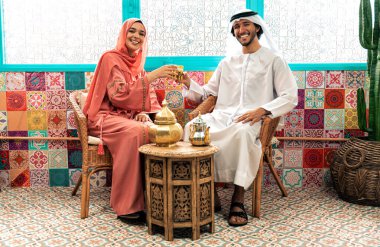 Emirati 'li genç bir çift geleneksel Arap kafesinde vakit geçiriyor. Kandura giyen kadın ve erkek Dubai 'den abaya sohbet ediyorlar..