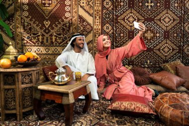 Emirati 'li genç bir çift geleneksel Arap kafesinde vakit geçiriyor. Kandura giyen kadın ve erkek Dubai 'den abaya sohbet ediyorlar..