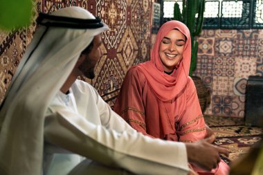 Emirati 'li genç bir çift geleneksel Arap kafesinde vakit geçiriyor. Kandura giyen kadın ve erkek Dubai 'den abaya sohbet ediyorlar..