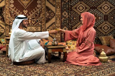 Emirati 'li genç bir çift geleneksel Arap kafesinde vakit geçiriyor. Kandura giyen kadın ve erkek Dubai 'den abaya sohbet ediyorlar..