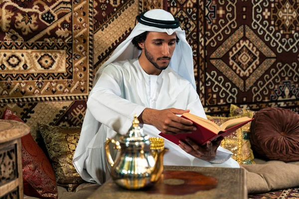 Emirati 'den kandura kıyafeti giyen bir adam Dubai' de geleneksel bir Arap evinde vakit geçiriyor.