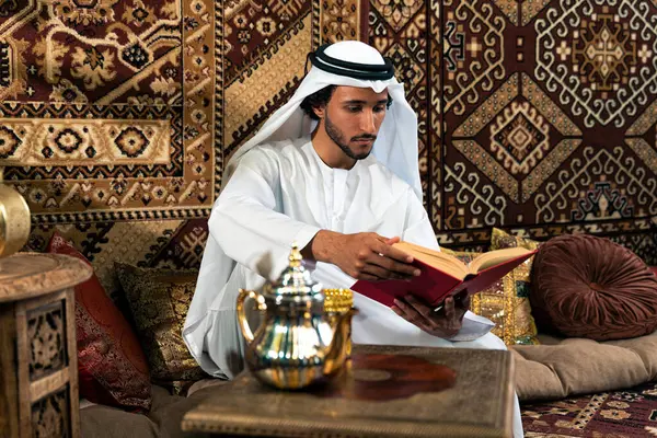 Emirati 'den kandura kıyafeti giyen bir adam Dubai' de geleneksel bir Arap evinde vakit geçiriyor.