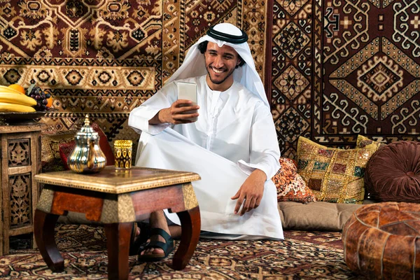 Emirati 'den kandura kıyafeti giyen bir adam Dubai' de geleneksel bir Arap evinde vakit geçiriyor.