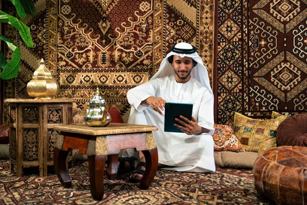 Emirati 'den kandura kıyafeti giyen bir adam Dubai' de geleneksel bir Arap evinde vakit geçiriyor.