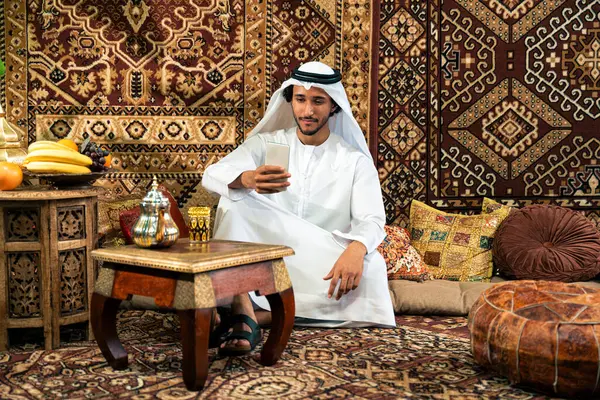 Emirati 'den kandura kıyafeti giyen bir adam Dubai' de geleneksel bir Arap evinde vakit geçiriyor.