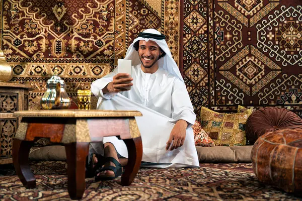 Emirati 'den kandura kıyafeti giyen bir adam Dubai' de geleneksel bir Arap evinde vakit geçiriyor.