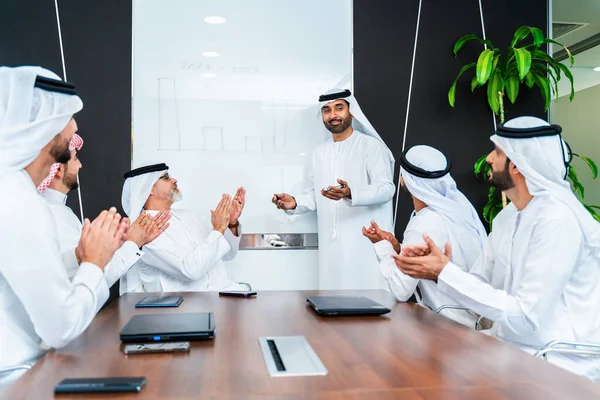 Group of corporate arab businessmen meeting in the office - Middle-eastern businesspeople wearing emirati kandora working in a meeting room, Dubai