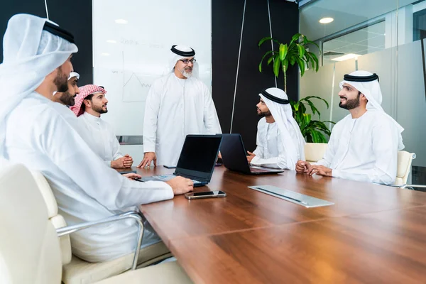 Group of corporate arab businessmen meeting in the office - Middle-eastern businesspeople wearing emirati kandora working in a meeting room, Dubai