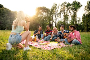 Çok ırklı bir grup genç parkta piknik yapmak için dışarıda zaman geçiriyorlar. Z kuşağı, yaşam tarzı ve arkadaşlık kavramları