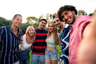 Çok ırklı bir grup genç parkta piknik yapmak için dışarıda zaman geçiriyorlar. Z kuşağı, yaşam tarzı ve arkadaşlık kavramları