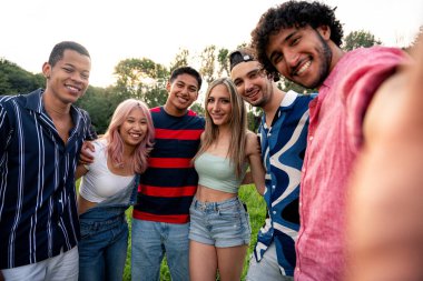 Çok ırklı bir grup genç parkta piknik yapmak için dışarıda zaman geçiriyorlar. Z kuşağı, yaşam tarzı ve arkadaşlık kavramları
