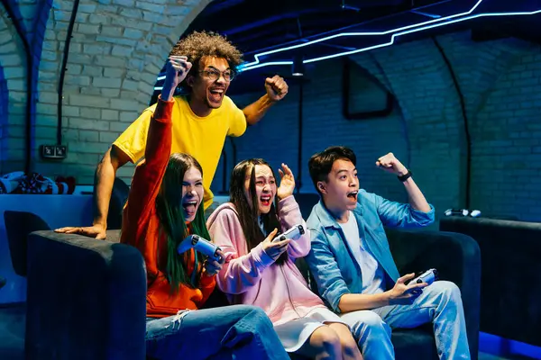 Kanepede oturmuş video oyunu oynayan çok ırklı bir grup genç arkadaş - Video oyuncular bilgisayar oyunu konsolunda e-spor yaparken eğleniyorlar