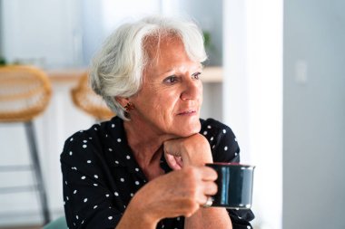Güzel, düşünceli, yaşlı, kır saçlı bir kadın bir fincan kahve içiyor genç, yaşlı bir büyükanne evde kaliteli zaman geçiriyor.