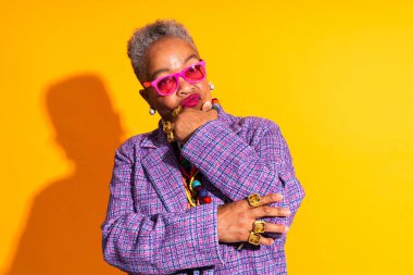 Stüdyoda izole edilmiş şık kıyafetler giyen komik yaşlı siyahi kadının renkli portresi - havalı yaşlı kadın yetişkin, yaşlılar, yaşlılar ve vücut pozitifliği kavramları