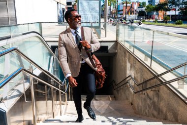 Şehirde gezen şık takım elbiseli, olgun siyahi işadamı, gri sakallı, yaşlı ve üst düzey bir erkek, metro ulaşımıyla seyahat ediyor.