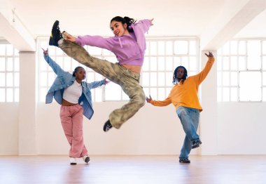 Çok ırklı hip-hop dansçılarından oluşan genç bir grup renkli sokak kıyafetleri giyip dans ediyorlar.