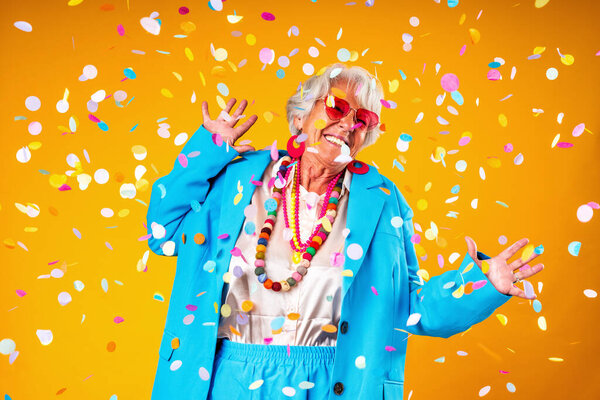 Красивая пожилая женщина с седыми волосами в красочной стильной одежде портрет в студии - веселая старая бабушка с модным стилем танцы под конфетти душ, чтобы отпраздновать день рождения