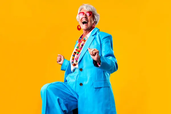 stock image Beautiful senior woman with gray hair wearing colorful stylish clothing portrait in studio - Cheerful old grandmother with fashionable style doing a joyful triumphant gesture