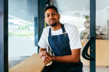 Fırın, kafede hamur işi, kahve ve fırında yemek servisi için hazır İspanyol siyahi bir adamın mutlu portresi. Restoran, kafe ve kendine güvenen garson barista servis, yardım ve hoş geldiniz.