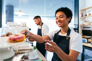 Pastane, kafede hamur işi, kahve ve fırında yemek servisi yapmaya hazır zenci erkek ve kadının mutlu portresi. Servis için tezgah, yardım ve bir kahve dükkanına hoş geldiniz.