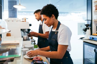 Pastane, kafede hamur işi, kahve ve fırında yemek servisi yapmaya hazır zenci erkek ve kadının mutlu portresi. Servis için tezgah, yardım ve bir kahve dükkanına hoş geldiniz.