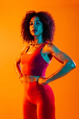 Sportif siyahi kadın spor kıyafetleri giyiyor spor salonunda, renkli dramatik ışıklandırma - spor yapan Afro-Amerikan bayan sporcu