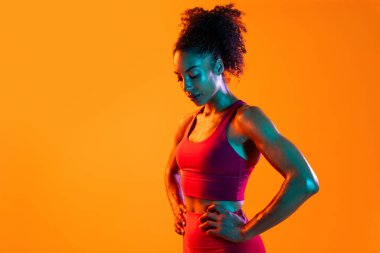 Sportif siyahi kadın spor kıyafetleri giyiyor spor salonunda, renkli dramatik ışıklandırma - spor yapan Afro-Amerikan bayan sporcu