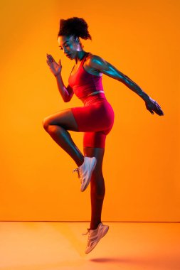 Sportif siyahi kadın spor kıyafetleri giyiyor spor salonunda, renkli dramatik ışıklandırma - spor yapan Afro-Amerikan bayan sporcu