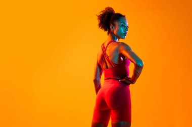Sportif siyahi kadın spor kıyafetleri giyiyor spor salonunda, renkli dramatik ışıklandırma - spor yapan Afro-Amerikan bayan sporcu