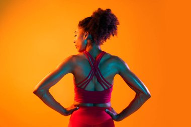 Sportif siyahi kadın spor kıyafetleri giyiyor spor salonunda, renkli dramatik ışıklandırma - spor yapan Afro-Amerikan bayan sporcu
