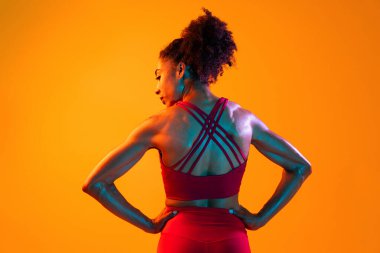 Sportif siyahi kadın spor kıyafetleri giyiyor spor salonunda, renkli dramatik ışıklandırma - spor yapan Afro-Amerikan bayan sporcu