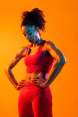 Sportif siyahi kadın spor kıyafetleri giyiyor spor salonunda, renkli dramatik ışıklandırma - spor yapan Afro-Amerikan bayan sporcu