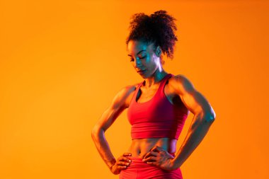 Sportif siyahi kadın spor kıyafetleri giyiyor spor salonunda, renkli dramatik ışıklandırma - spor yapan Afro-Amerikan bayan sporcu