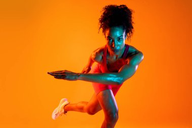 Sportif siyahi kadın spor kıyafetleri giyiyor spor salonunda, renkli dramatik ışıklandırma - spor yapan Afro-Amerikan bayan sporcu