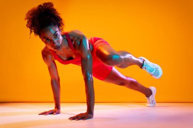 Sportif siyahi kadın spor kıyafetleri giyiyor spor salonunda, renkli dramatik ışıklandırma - spor yapan Afro-Amerikan bayan sporcu
