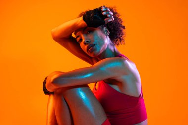 Sportif siyahi kadın spor kıyafetleri giyiyor spor salonunda, renkli dramatik ışıklandırma - spor yapan Afro-Amerikan bayan sporcu