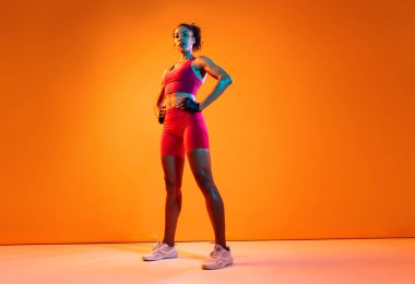 Sportif siyahi kadın spor kıyafetleri giyiyor spor salonunda, renkli dramatik ışıklandırma - spor yapan Afro-Amerikan bayan sporcu