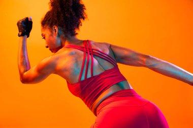 Sportif siyahi kadın spor kıyafetleri giyiyor spor salonunda, renkli dramatik ışıklandırma - spor yapan Afro-Amerikan bayan sporcu