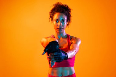 Sportif siyahi kadın spor kıyafetleri giyiyor spor salonunda, renkli dramatik ışıklandırma - spor yapan Afro-Amerikan bayan sporcu