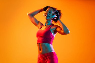 Sportif siyahi kadın spor kıyafetleri giyiyor spor salonunda, renkli dramatik ışıklandırma - spor yapan Afro-Amerikan bayan sporcu