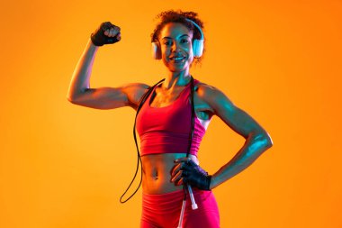 Sportif siyahi kadın spor kıyafetleri giyiyor spor salonunda, renkli dramatik ışıklandırma - spor yapan Afro-Amerikan bayan sporcu