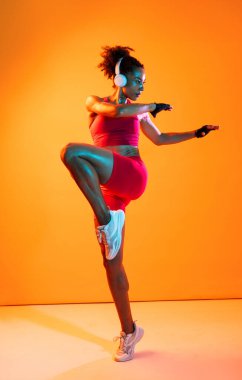 Sportif siyahi kadın spor kıyafetleri giyiyor spor salonunda, renkli dramatik ışıklandırma - spor yapan Afro-Amerikan bayan sporcu