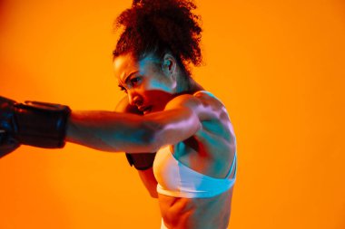 Sportif siyahi kadın spor kıyafetleri giyiyor spor salonunda, renkli dramatik ışıklandırma - spor yapan Afro-Amerikan bayan sporcu