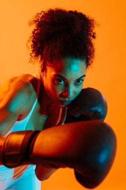 Sportif siyahi kadın spor kıyafetleri giyiyor spor salonunda, renkli dramatik ışıklandırma - spor yapan Afro-Amerikan bayan sporcu