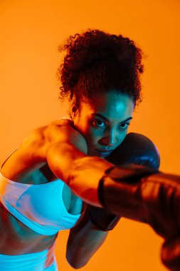 Sportif siyahi kadın spor kıyafetleri giyiyor spor salonunda, renkli dramatik ışıklandırma - spor yapan Afro-Amerikan bayan sporcu