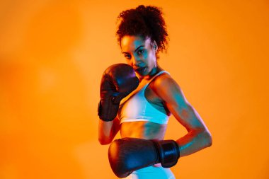 Sportif siyahi kadın spor kıyafetleri giyiyor spor salonunda, renkli dramatik ışıklandırma - spor yapan Afro-Amerikan bayan sporcu