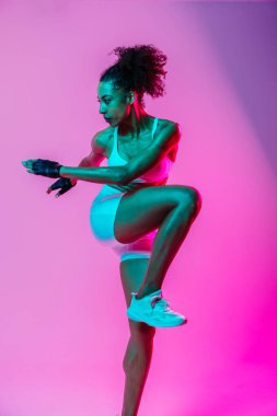Sportif siyahi kadın spor kıyafetleri giyiyor spor salonunda, renkli dramatik ışıklandırma - spor yapan Afro-Amerikan bayan sporcu