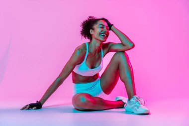 Sportif siyahi kadın spor kıyafetleri giyiyor spor salonunda, renkli dramatik ışıklandırma - spor yapan Afro-Amerikan bayan sporcu