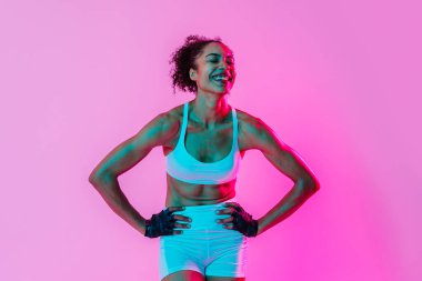 Sportif siyahi kadın spor kıyafetleri giyiyor spor salonunda, renkli dramatik ışıklandırma - spor yapan Afro-Amerikan bayan sporcu